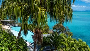 A pool area with a view of the ocean, surrounded by lush greenery and palm trees. - Edge 10 - Magnificent Views! (Hamilton Island)