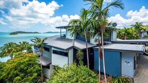 A modern house with a large balcony overlooking a body of water, surrounded by lush greenery. - Edge 10 - Magnificent Views! (Hamilton Island)