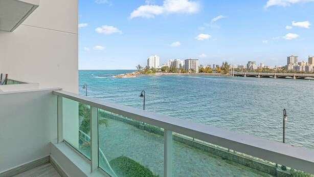 A balcony with a view of a coastal cityscape, clear blue water, and a distant beach. - Sunset Studio | located at Condado Lagoon Villas (Condado Lagoon Villas)