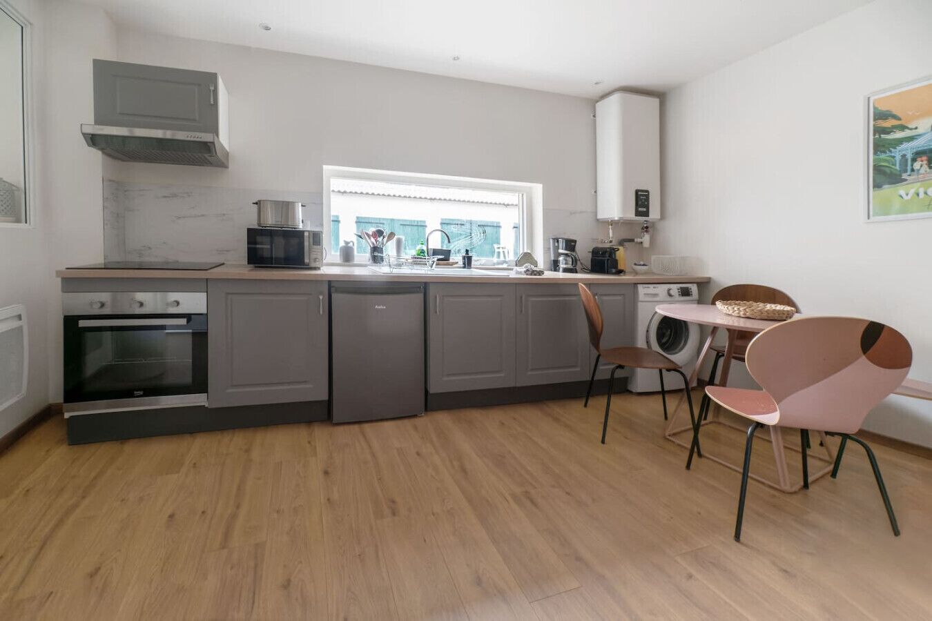 Una cocina compacta con horno empotrado, microondas y lavavajillas, una ventana con vistas, y un comedor con sillas variadas.