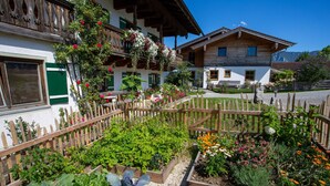 Uma casa de madeira tradicional com varanda, rodeada por um jardim bem cuidado com diversas plantas e flores.