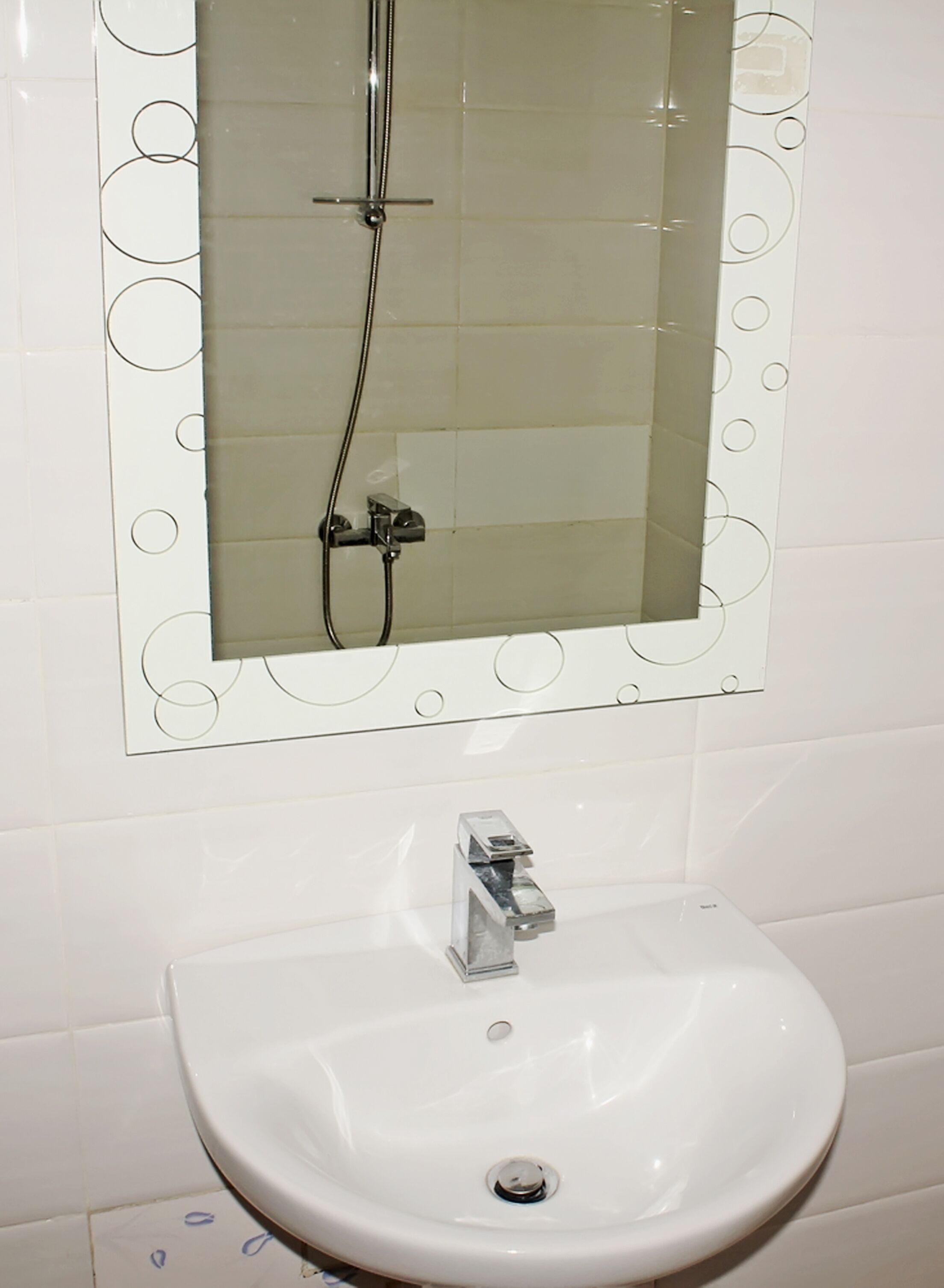 Un baño con un lavabo blanco, un espejo con diseños circulares y una ducha.
