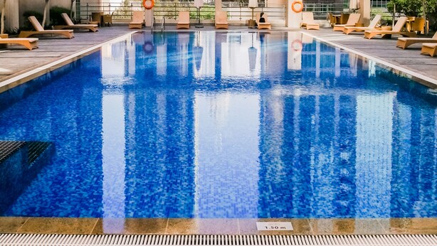 En swimmingpool med solstolar och parasoller, omgiven av höga byggnader.