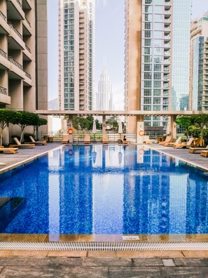 A swimming pool with lounge chairs and umbrellas, surrounded by high-rise buildings. - Nasma Luxury Stays- BLVD Central Podium (Dubai)