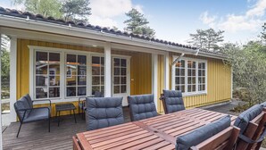 Eine Holzterrasse mit Tisch und Stühlen, eine überdachte Veranda mit einer gelben Außenwand und großen Fenstern.