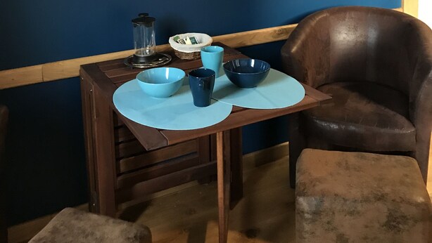 Een eetgedeelte met een tafel gedekt voor twee personen, een stoel en een afbeelding van een strand op de muur.