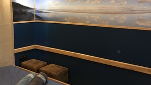 Een kamer met een bed, een wandplank en een schilderij van een strandgezicht.