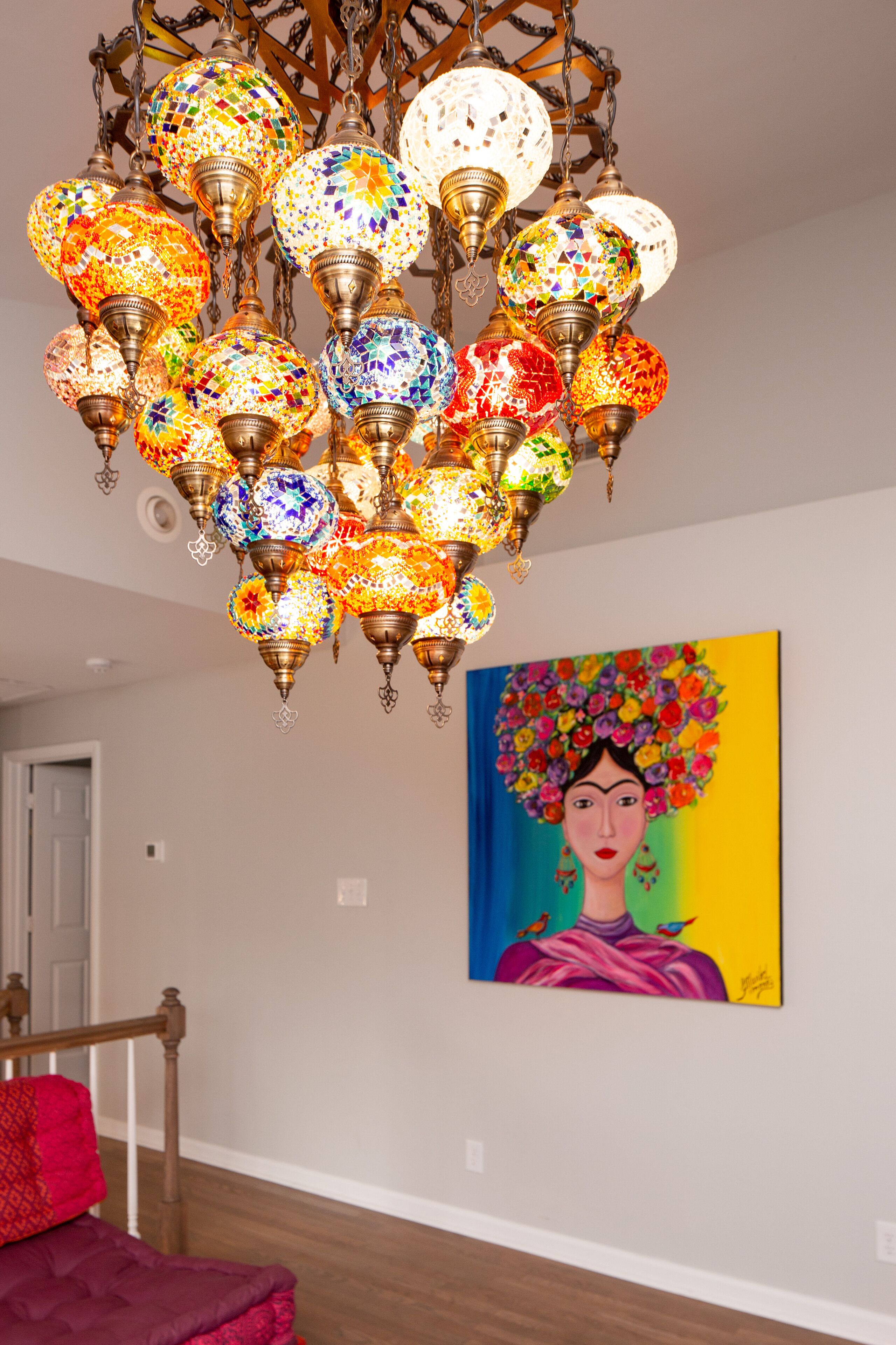 Un lustre orné de sphères de verre colorées, un tableau accroché au mur et un lit avec une tête de lit en bois.