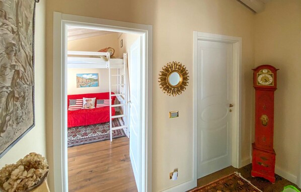 Une pièce avec un lit superposé, un canapé rouge, un miroir, une horloge et une porte.