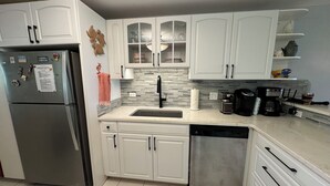 A modern kitchen with white cabinets, a stainless steel refrigerator, a dishwasher, and a coffee maker.