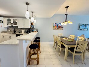 A modern kitchen with white cabinets, a central island with stools, and a dining area with a table and chairs.