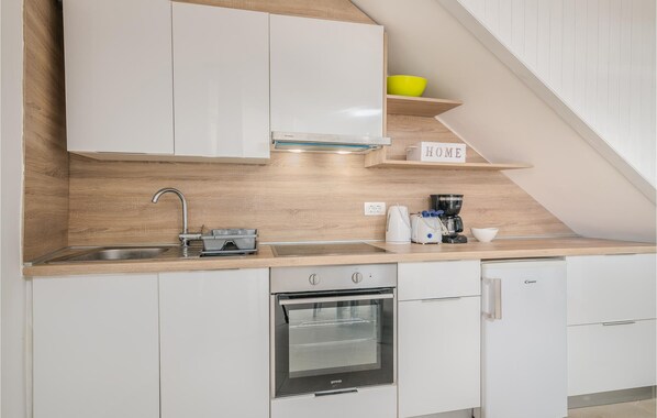 A modern kitchen with white cabinets, a stainless steel sink, a built-in oven, and a coffee maker on the countertop.