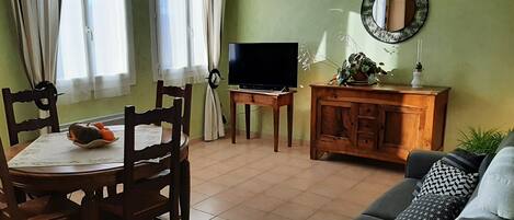 A living room with a dining table, chairs, a sofa, a TV, a cabinet, and a clock on the wall.