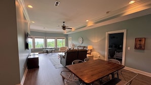 A spacious living room with a wooden dining table, comfortable seating, a ceiling fan, and a view of the outdoors. - Creekview Manor (Burkesville)
