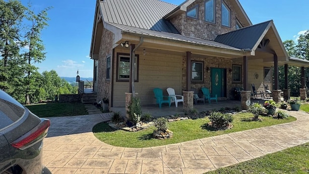 A two-story house with a stone facade, a covered porch with chairs, and a car parked in the driveway. - Creekview Manor (Burkesville)