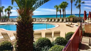 A pool area with lounge chairs and palm trees, overlooking a beach.