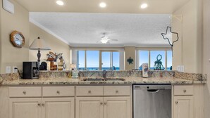 A kitchen with a dishwasher, a clock, and a view of the ocean.