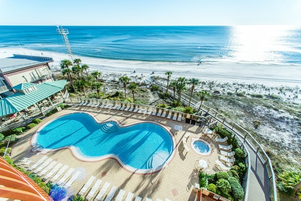 Un complexe hôtelier dot é d’une grande piscine, de chaises longues et offrant une vue sur la plage et l’océan.
