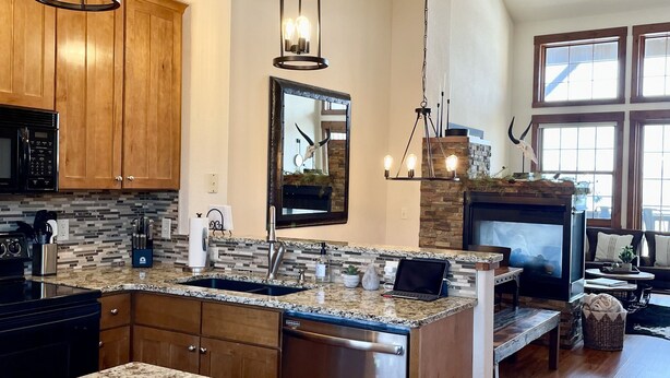 A spacious kitchen with granite countertops, wooden cabinets, and a large island. There is a built-in microwave, a sink, and a stove. The kitchen is well-lit with pendant lights and has a stone backsplash. - Steps away from the lift - Ski, Bike, Golf, Fish - Four Season's of Family fun! (Granby)