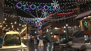 A covered outdoor area with string lights and star decorations, a car, and a person with a shopping bag. - Steps away from the lift - Ski, Bike, Golf, Fish - Four Season's of Family fun! (Granby)
