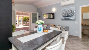 A dining area with a dark wooden table, white chairs, a vase with flowers, and a painting of a tree on the wall. - Sunset Bay Pool Villa Sardinia Heated Swimming Private Pool with Whirlpool (Valledoria)