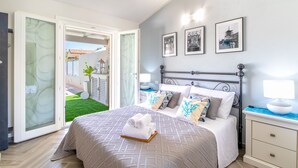 A bedroom with a bed, a nightstand, a lamp, and a view of a garden through a sliding door. - Sunset Bay Pool Villa Sardinia Heated Swimming Private Pool with Whirlpool (Valledoria)