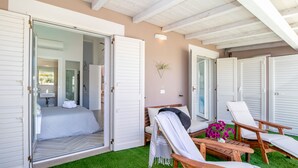 A bedroom with a bed, a bathroom, and a seating area with chairs and a table. - Sunset Bay Pool Villa Sardinia Heated Swimming Private Pool with Whirlpool (Valledoria)