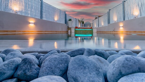 A pool area with a clear view of the water, a stone border, and a sunset sky. - Sunset Bay Pool Villa Sardinia Heated Swimming Private Pool with Whirlpool (Valledoria)