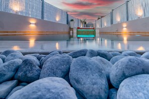 Un espace piscine offrant une vue dégagée sur l’eau, bordé de pierres, avec un ciel au coucher du soleil.