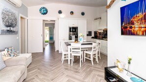 A modern living room with a sofa, a dining table with chairs, a kitchen area with cabinets and appliances, and a hallway leading to another room. - Sunset Bay Pool Villa Sardinia Heated Swimming Private Pool with Whirlpool (Valledoria)