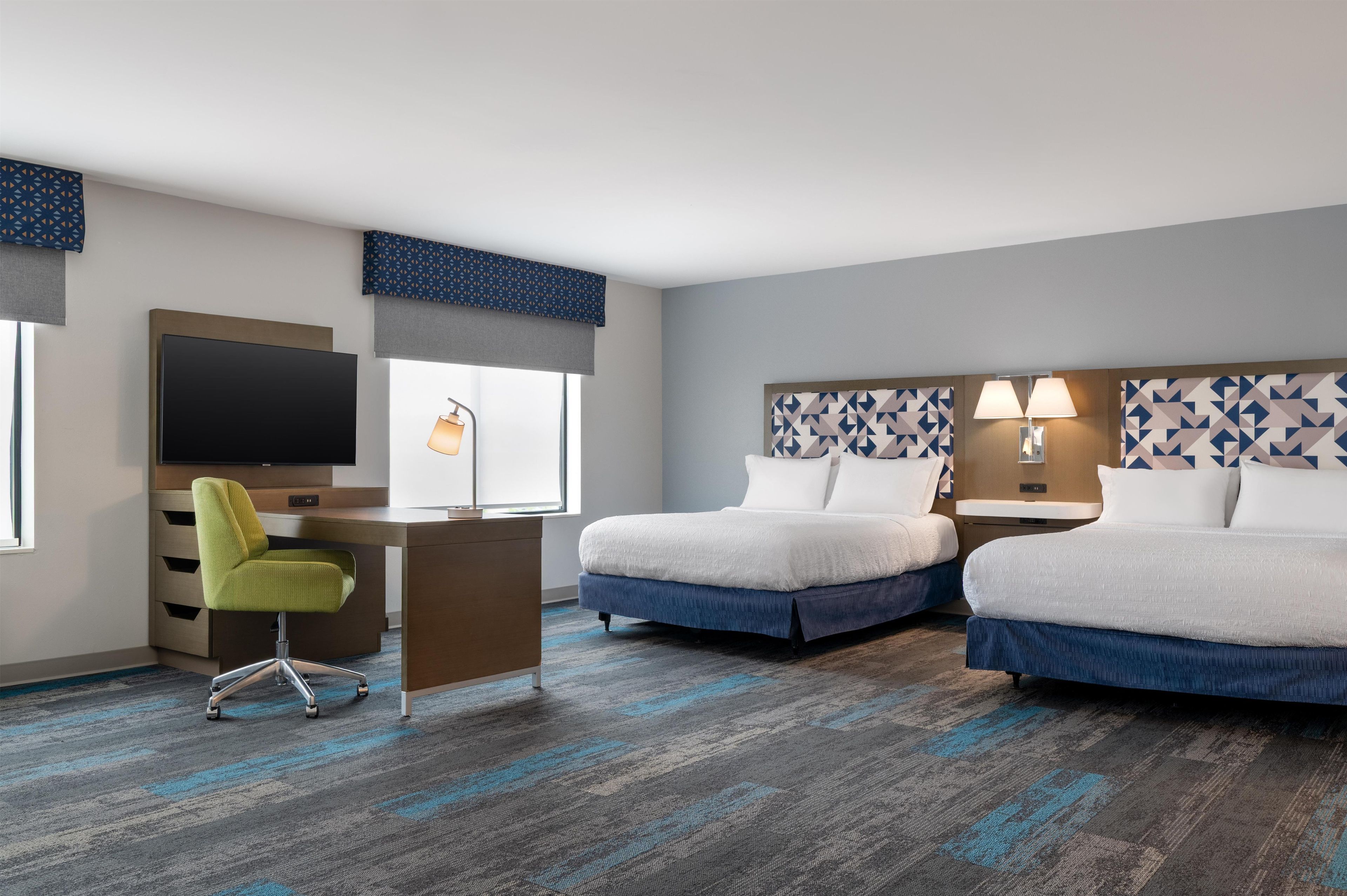 A hotel room with a bed, a desk, a chair, a TV, and a window.