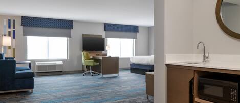 Habitación de hotel con cama, escritorio, silla, televisor y baño con lavamanos y espejo.