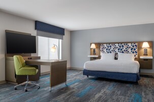Una habitación de hotel con cama, escritorio, televisión y una silla.