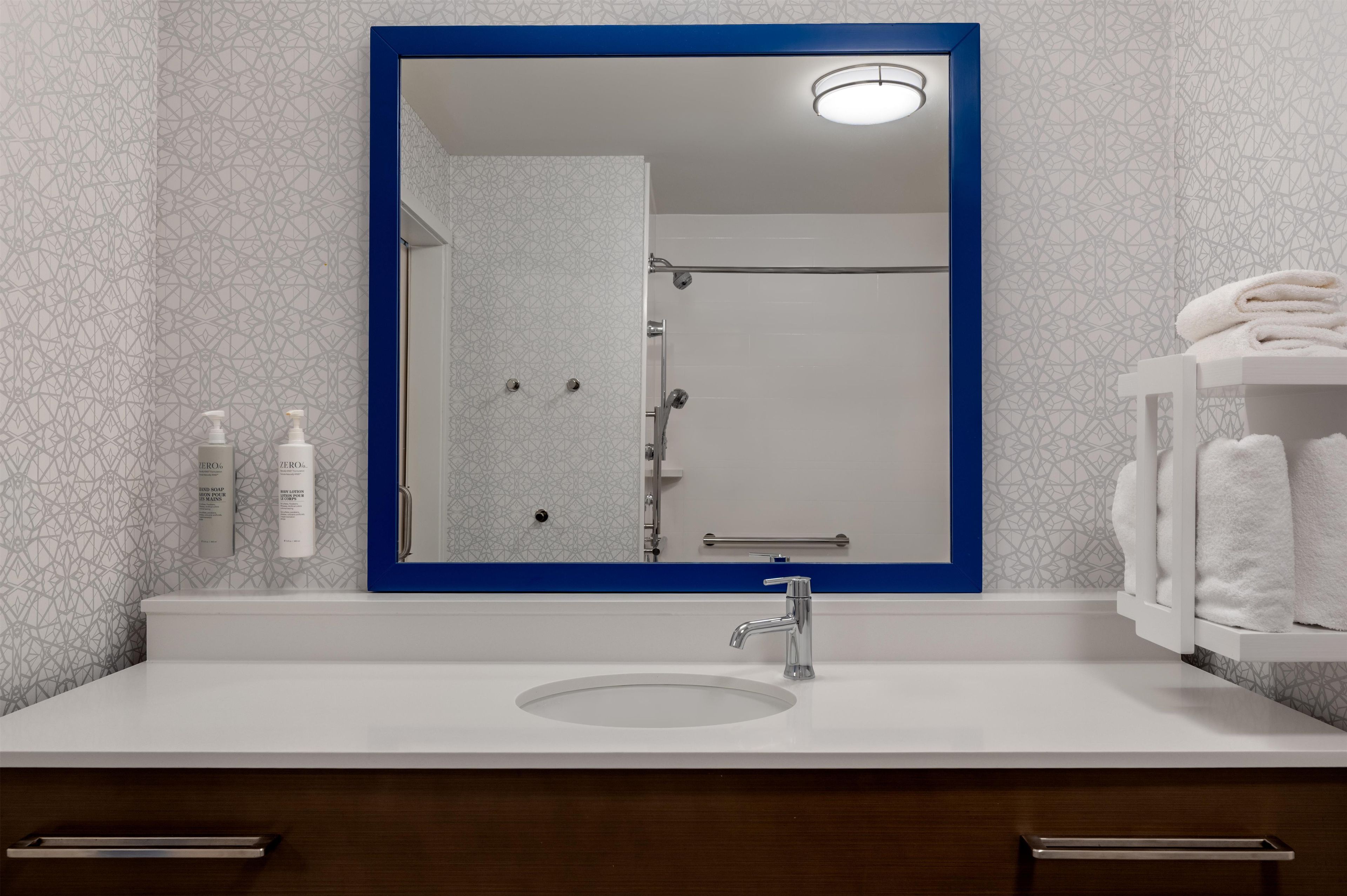 Un baño con un lavamanos blanco, un espejo con marco azul y un perchero.