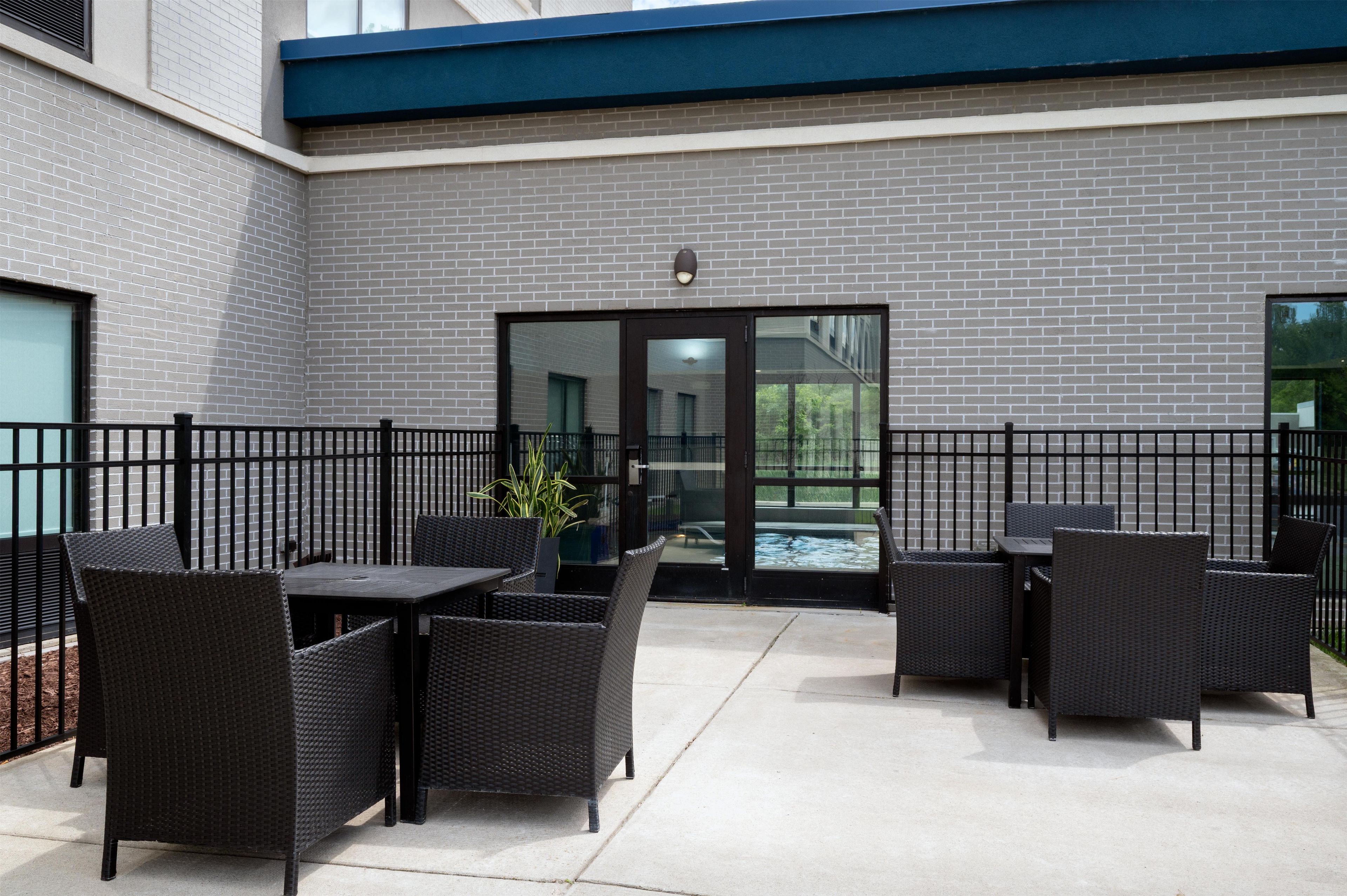 An outdoor patio area with a brick wall, a glass door entrance, and black wicker furniture.