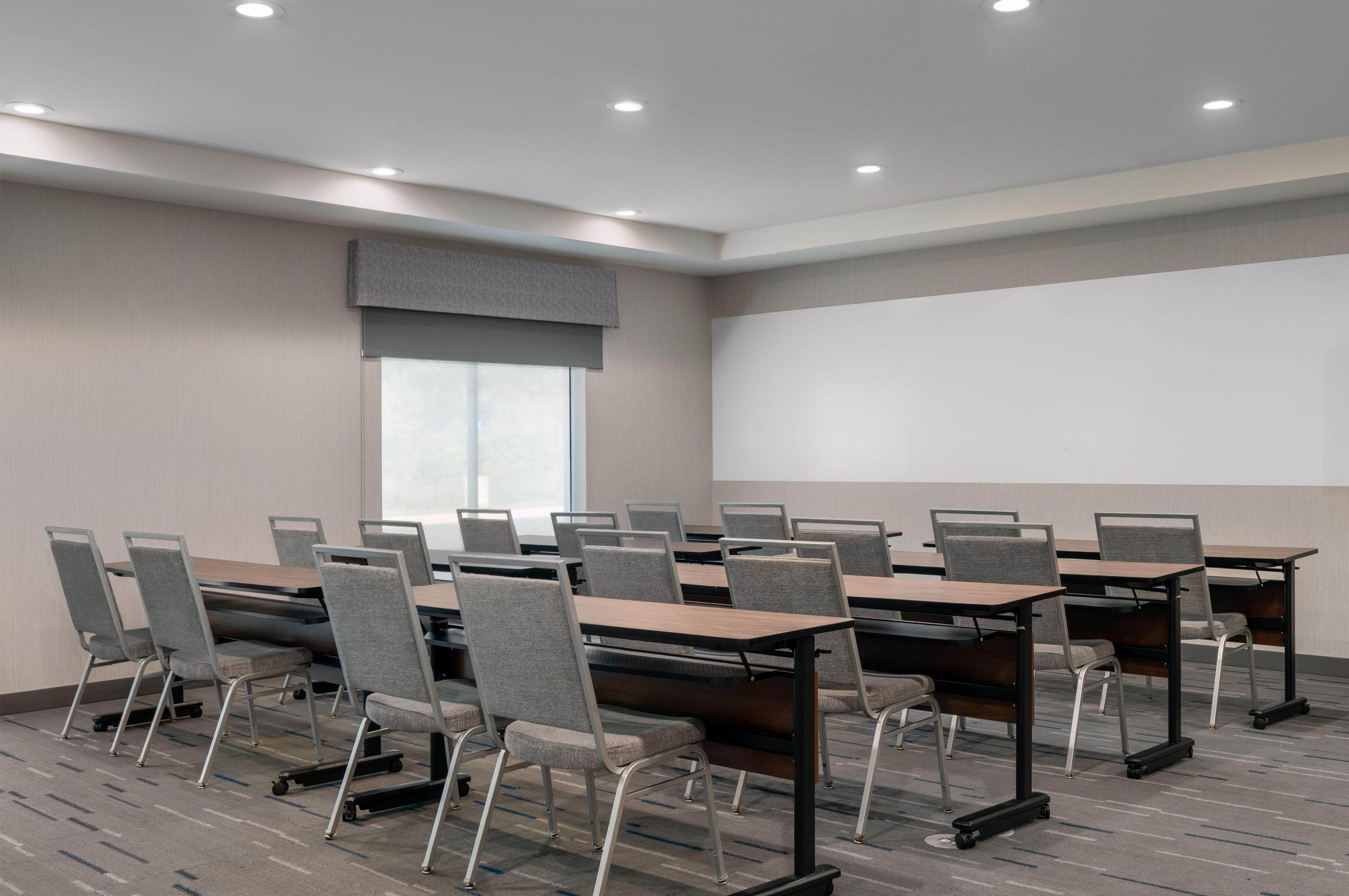 Uma sala de conferências com um amplo projetor, várias mesas e cadeiras.