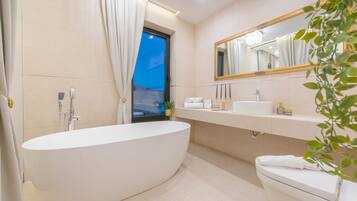 Un baño moderno con una bañera independiente, un espejo grande, un lavabo y un inodoro.