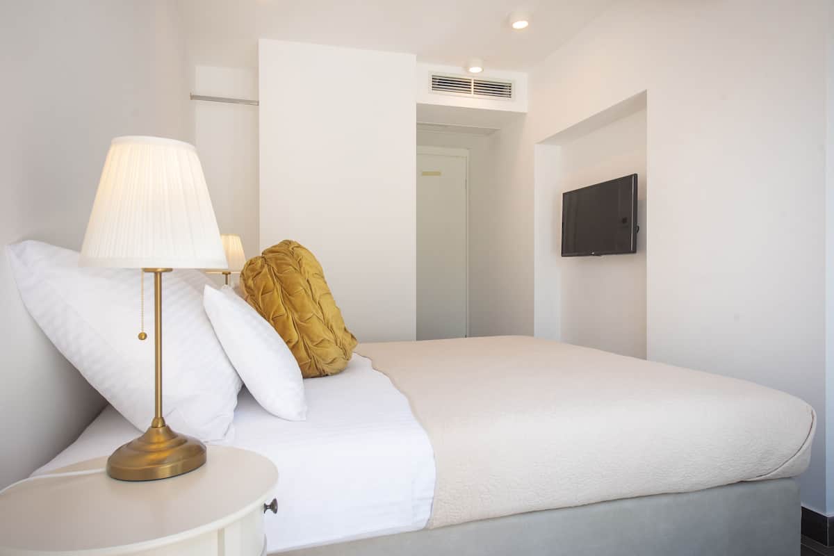 A neatly made bed with white bedding, a gold-colored throw pillow, and a bedside lamp.