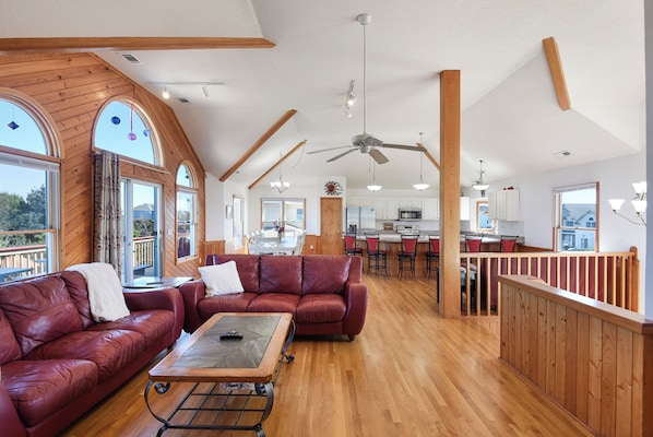 A spacious living area with a red leather sofa, a wooden coffee table, and a dining area with a kitchen in the background.