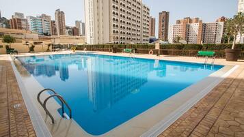 Una piscina con agua cristalina azul, rodeada por un deck empedrado y una barandilla de metal.