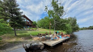 A wooden dock extending into a river with a picnic table and lounge chairs.