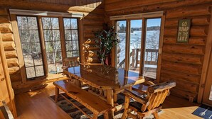 A wooden cabin with a large dining table and benches, large windows with a view of a lake, and a sign that says "GO JUMP IN THE LAKE".