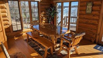 Une cabane en bois avec une grande table à manger et des bancs, de grandes fenêtres donnant sur un lac, et une pancarte sur laquelle on peut lire : « ALLEZ, SAUTEZ DANS LE LAC ! »