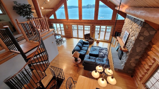 A spacious cabin with a high ceiling, large windows, a cozy living area with a sofa and a dining table, and a stone fireplace.