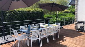 An outdoor dining area with white chairs and tables, two large umbrellas, and a wooden deck. - Maison Familiale 7ch au Coeur de Ste Marine. Plage à 10m à Pieds ou 5 en Vélos ! (Combrit)