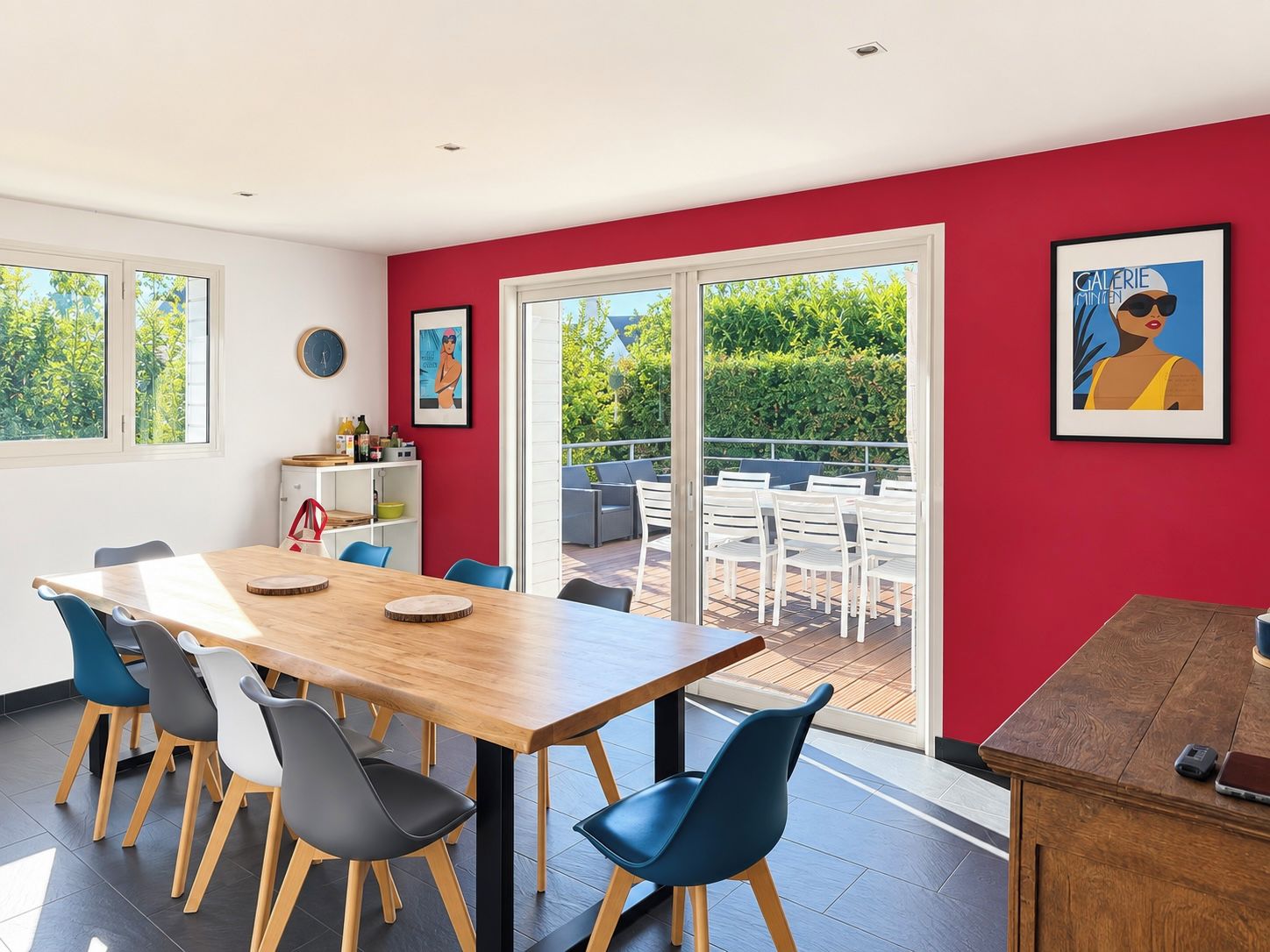Un comedor moderno con mesa y sillas de madera, una pared de acento roja y vistas al exterior.