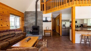 A cozy cabin interior with a wooden interior, a stone fireplace, a sofa, a dining table, and a kitchen area. - Southgate Getaway of Yosemite (Fish Camp)