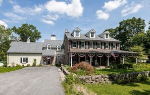 A large, two-story house with a stone facade, a covered porch, and a flag. - Private, Fully Renovated 1 bedroom Carriage House (Phoenixville)