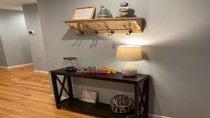 Un couloir avec une console en bois foncé, une étagère murale ornée d’objets décoratifs et un lampadaire.