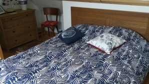 Una cama con una colcha estampada, un cabecero de madera y una silla roja al fondo.